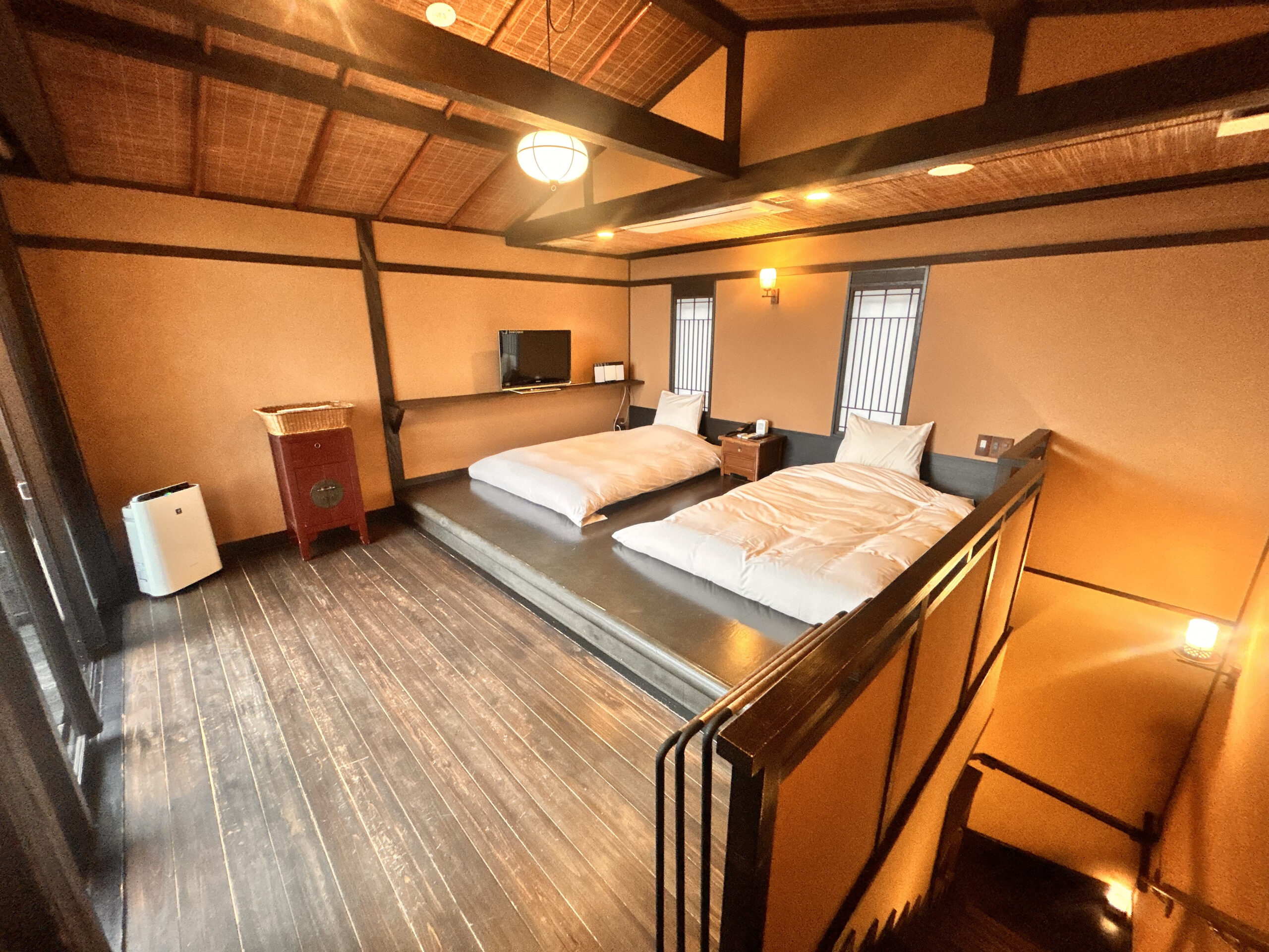 雪タイプ2階寝室の引き（ベッド2台＋屋根裏天井＋木の階段、暖色照明の隠れ宿らしい雰囲気）